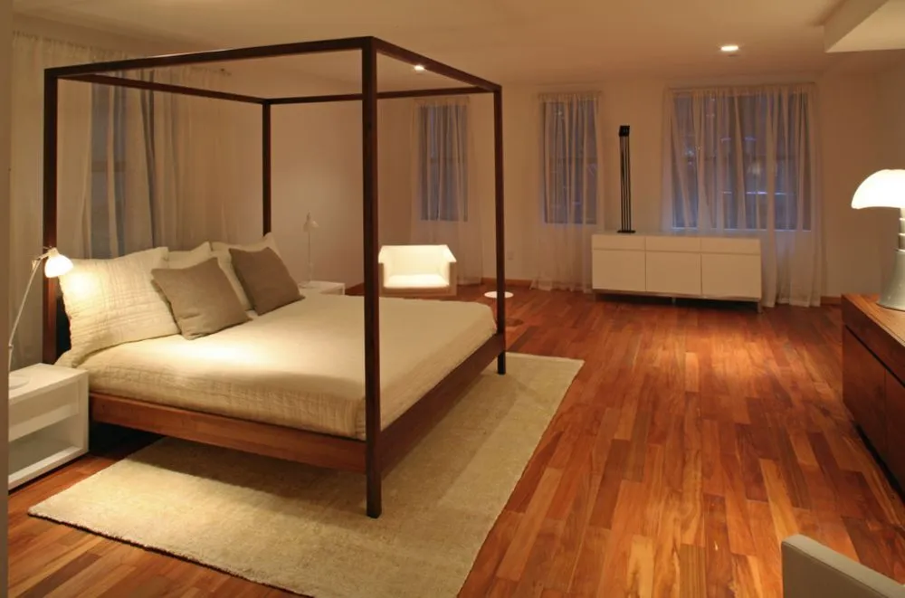 Minimal bedroom with a dark four-poster bed on warm wood floors