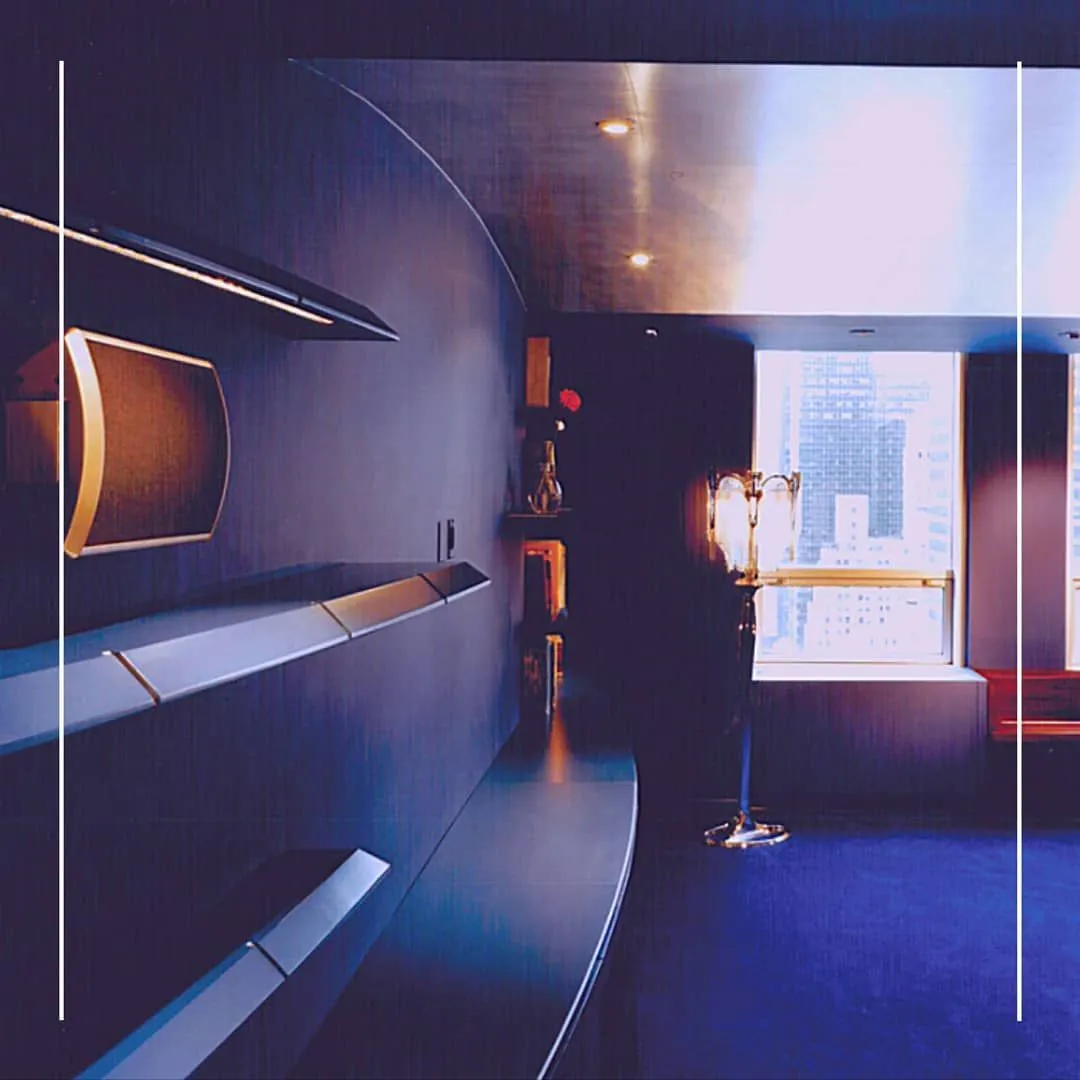 Curved blue-lit interior wall with built-in shelving and a city-view window