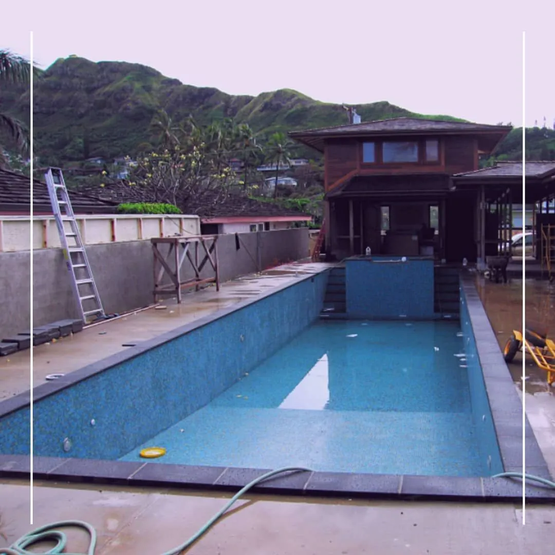 Lap pool under construction beside a timber house below green mountains