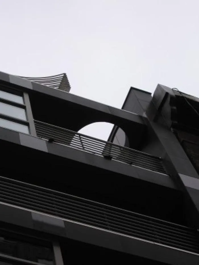 Upward view of dark metal balconies with a circular cutout against the sky