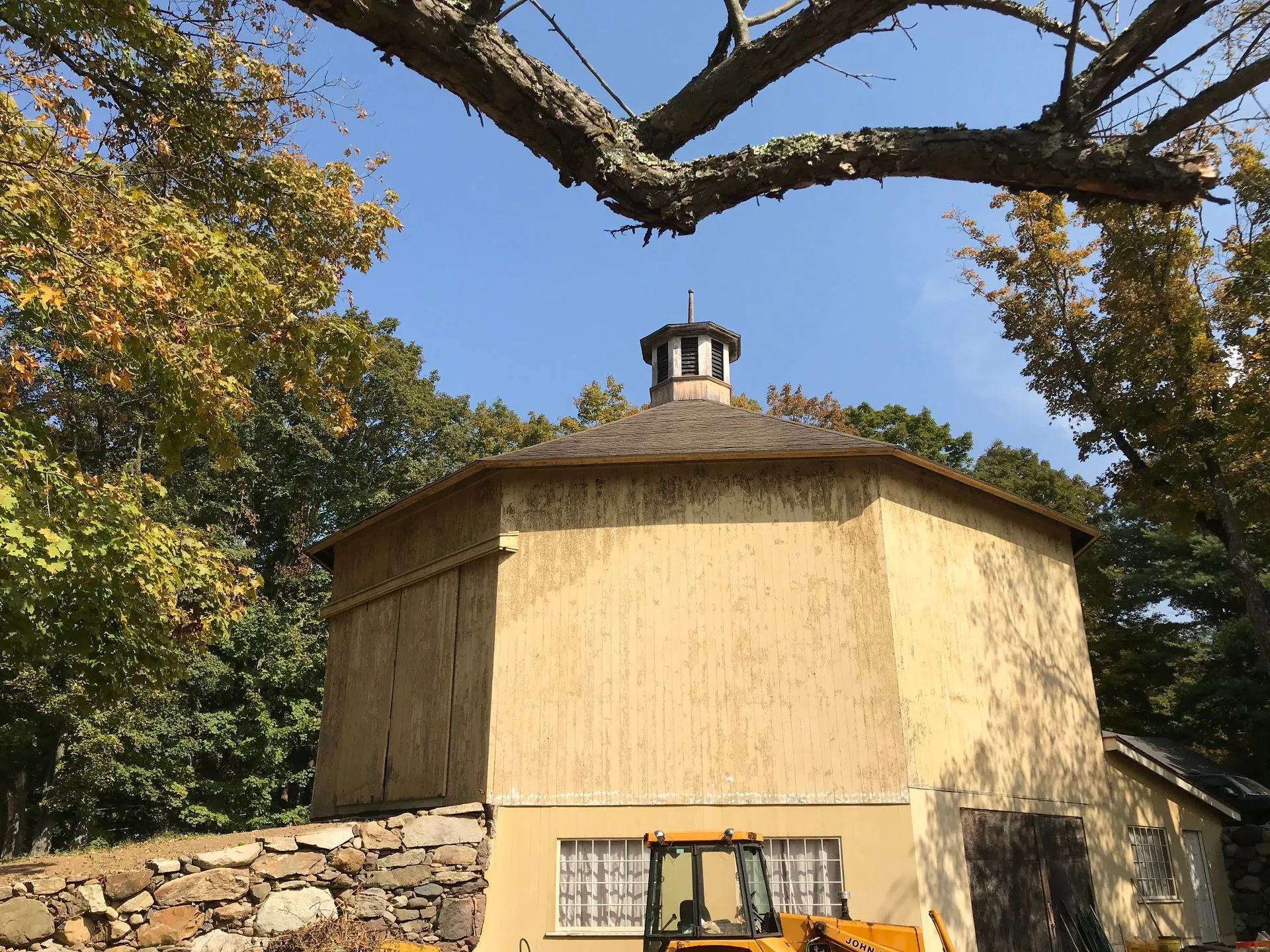 Octagonal barn with a cupola on a fieldstone base, framed by an overhanging branch