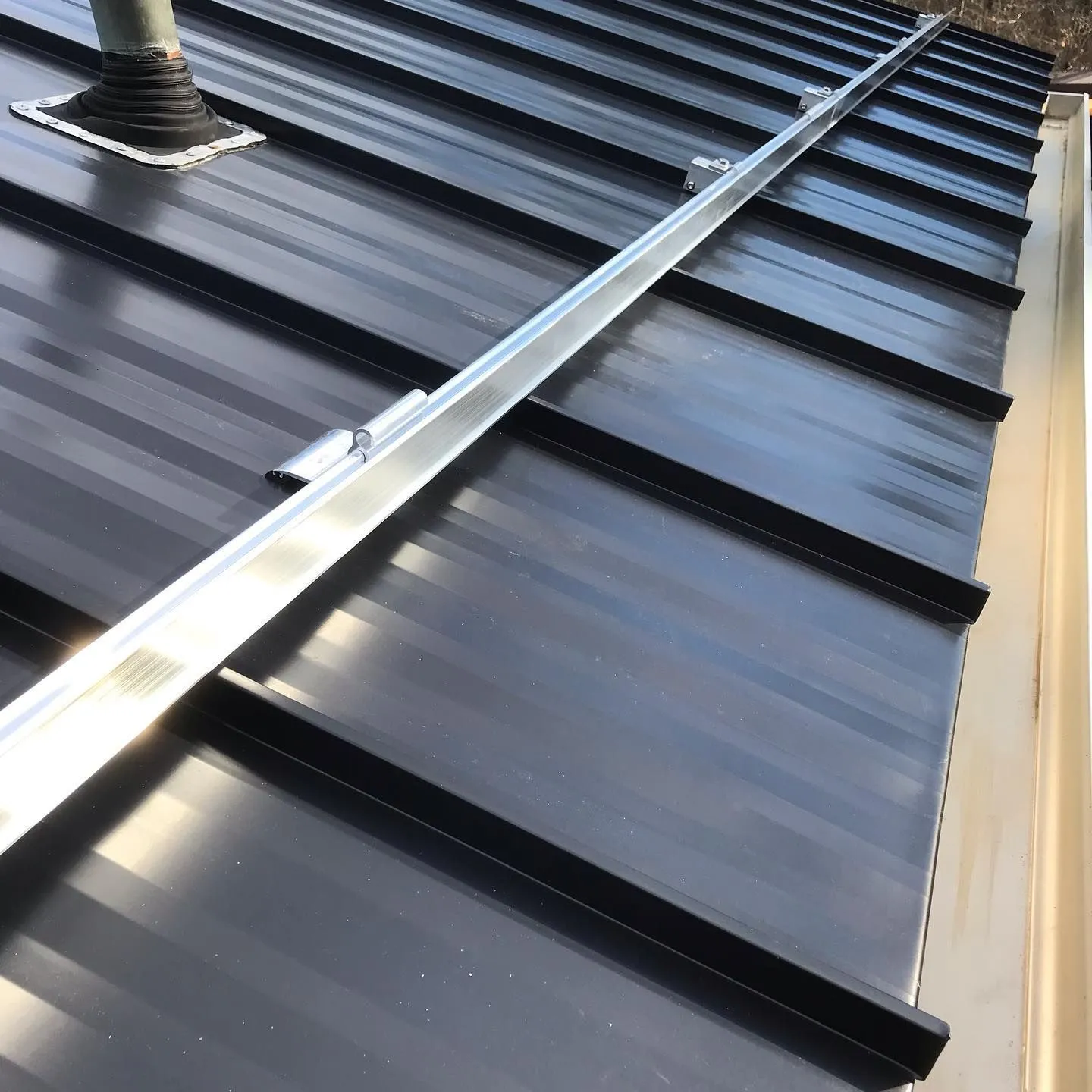 Standing-seam black metal roof with a pipe flashing and snow rail